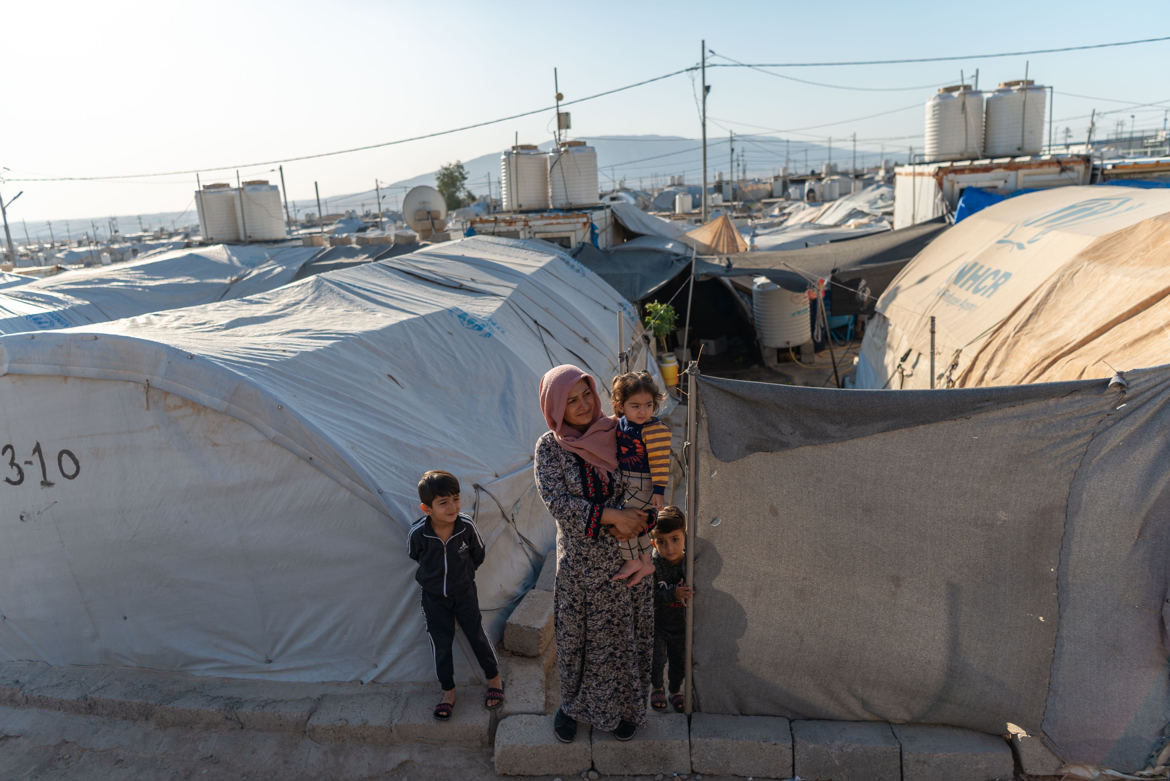 Woman stands with her children in a refugee camp.