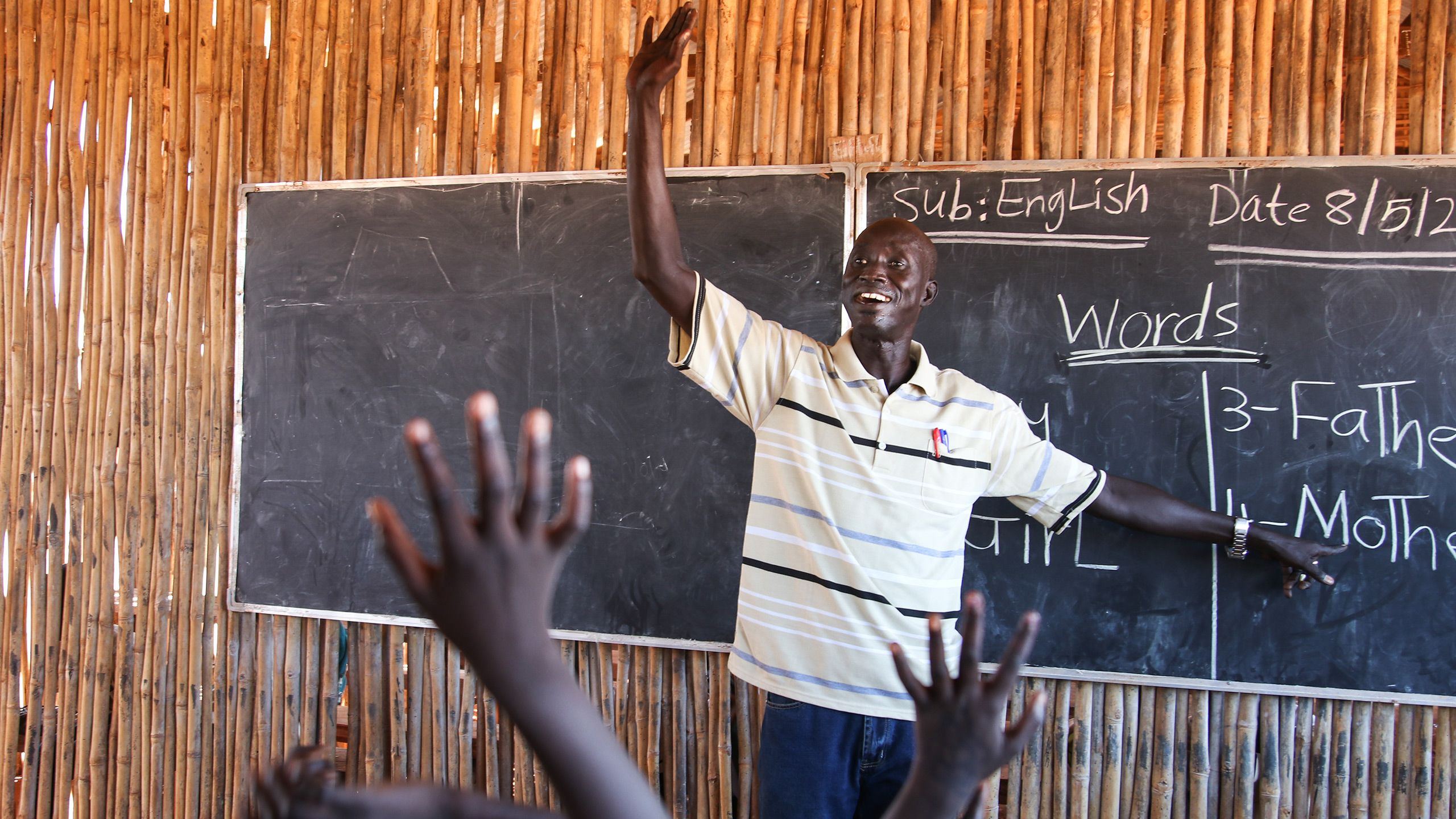 A man standing in front of the black board in a classroom.