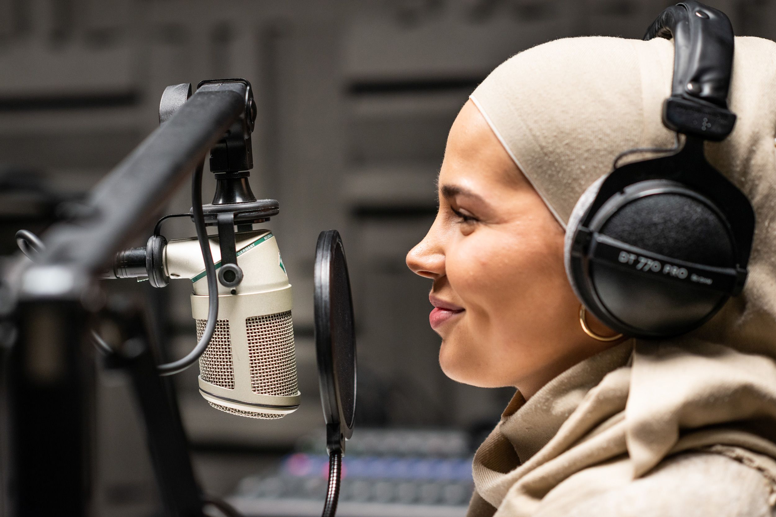 Iman Meskini sitter foran en podkast-mikrofon og smiler.