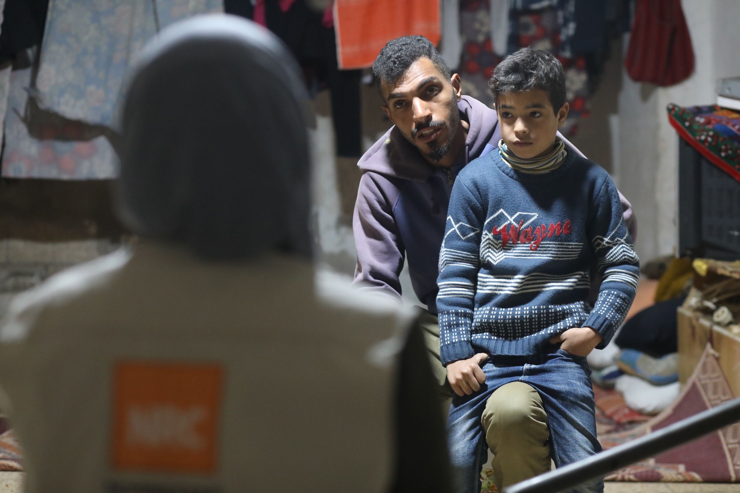 A boy sits on his father's lap and talks with an aid worker.