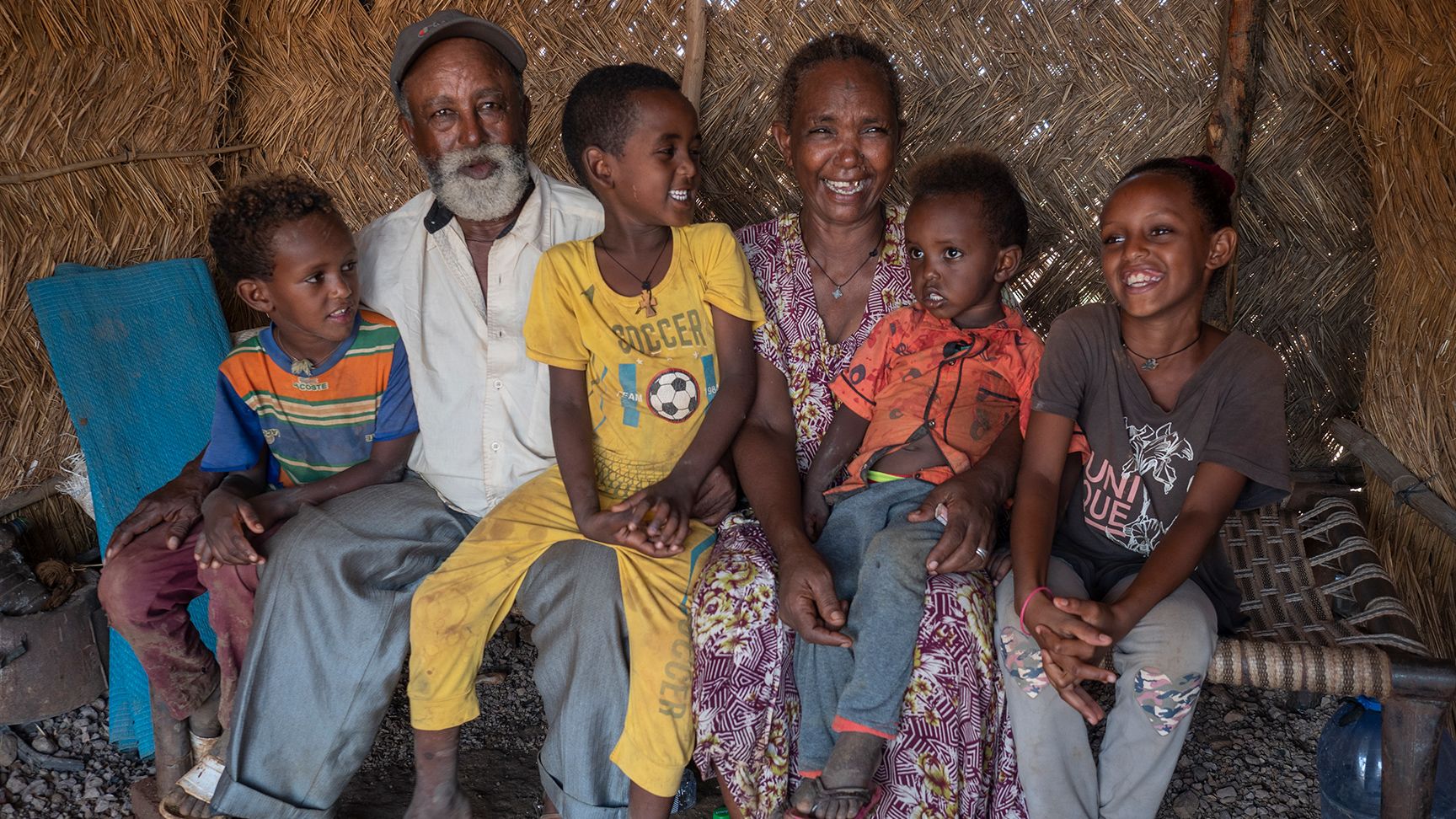 Two grandparents surrounded by four grandchildren. They are holding around each other and laughing.
