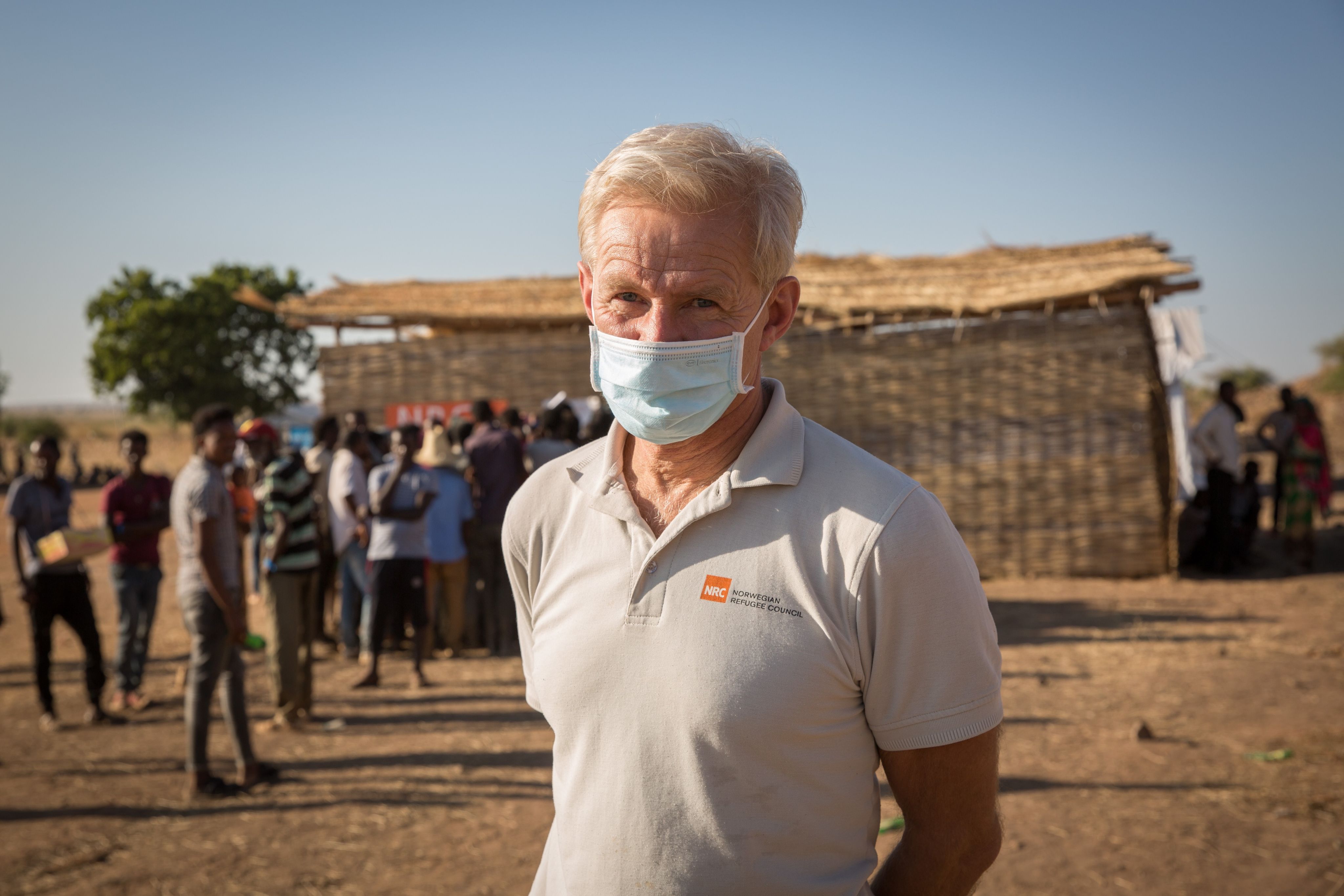Jan Egeland, a man with grey hair, is wearing a face mask and a light polo shirt bearing the Norwegian Refugee Council's logo.