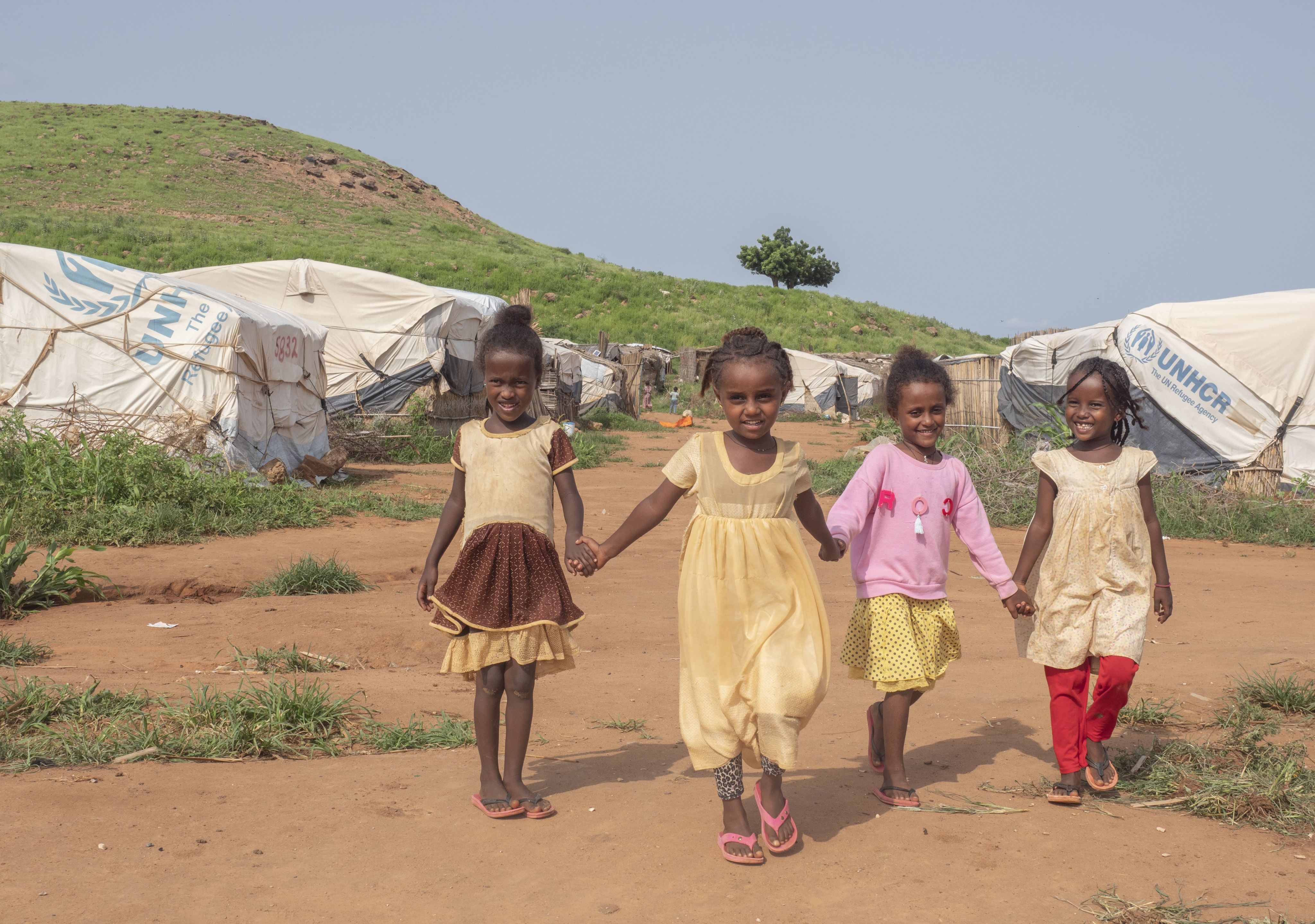 Four young girls hold hands and run towards the camera laughing.