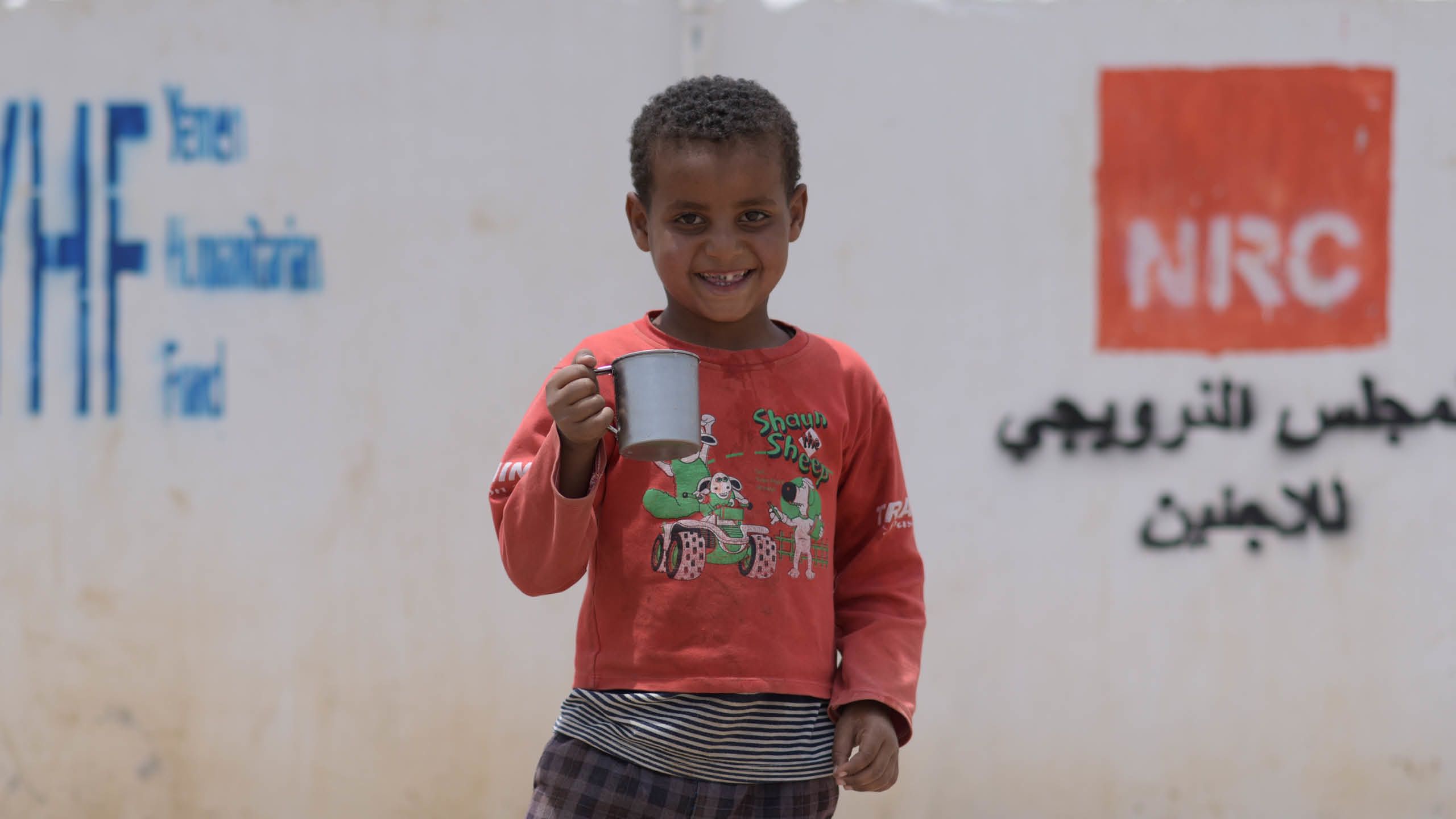 Little boy in a red sweater, smiling and holding a cup