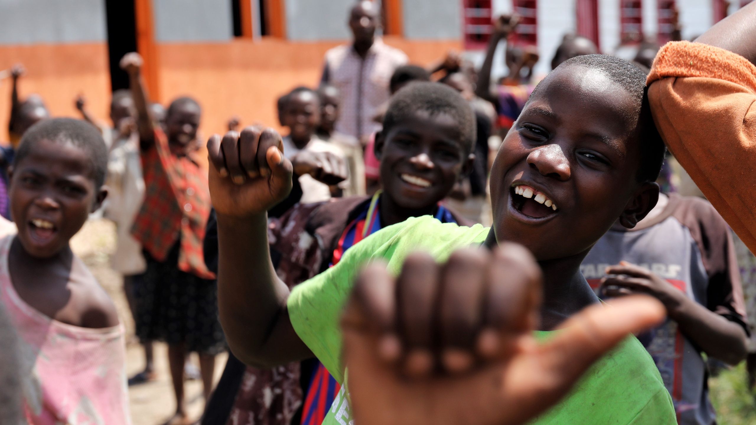 A group of children smiling and waving to the camera.