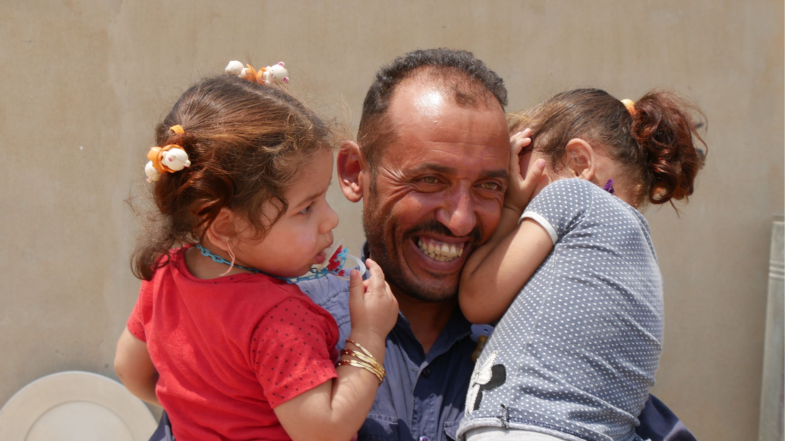 A man smiling wide, carrying his two daughters