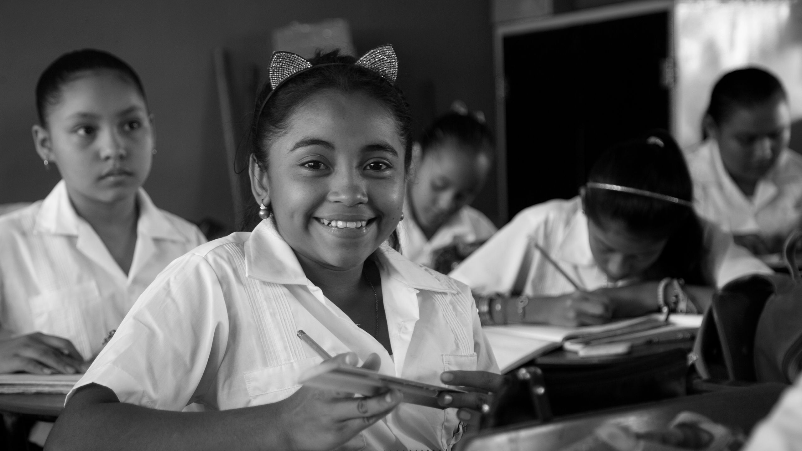 Sandy smiling to the camera. She is wearing a white school uniform and a head band with cat ears.