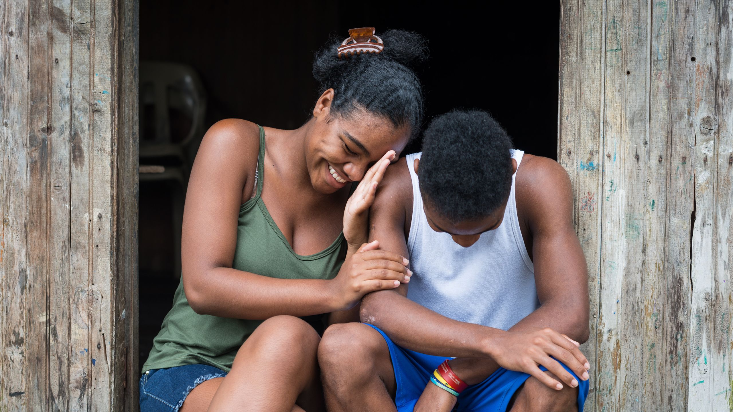 Leidy and her little brother sitting next to each other, laughing.
