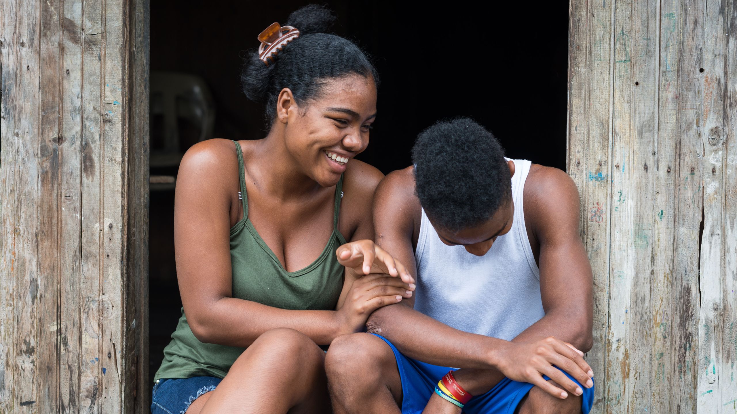 Leidy and her little brother sitting next to each other, laughing.