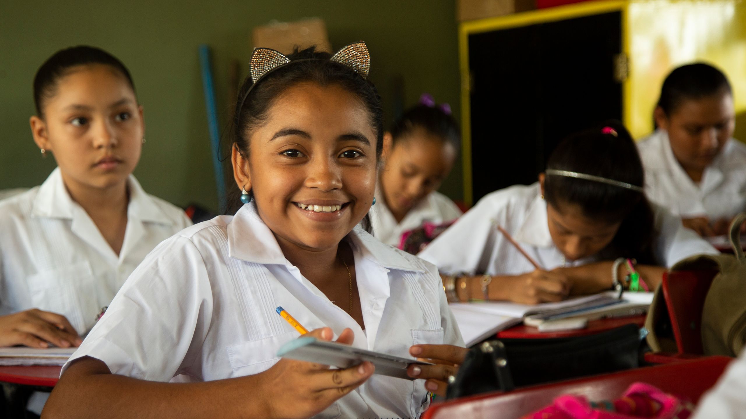 Sandy smiling to the camera. She is wearing a white school uniform and a head band with cat ears.