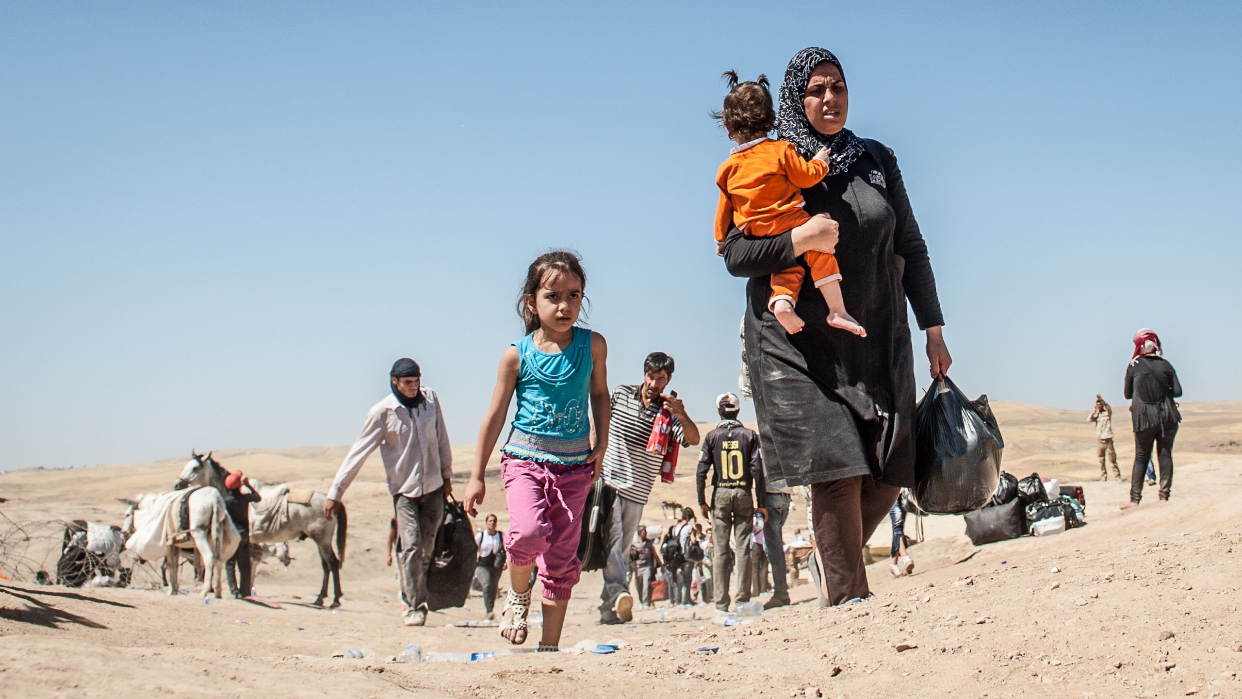 En liten jente og kvinne som bærer et barn på armen krysser grensen inn til Irak fra Syria.