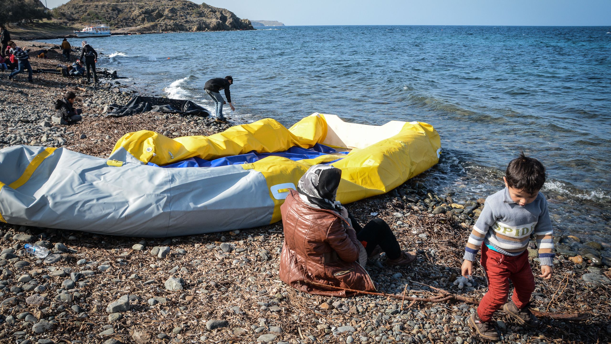 En kvinne sitter på stranden ved siden av en stor, gul gummibåt med lite luft.
