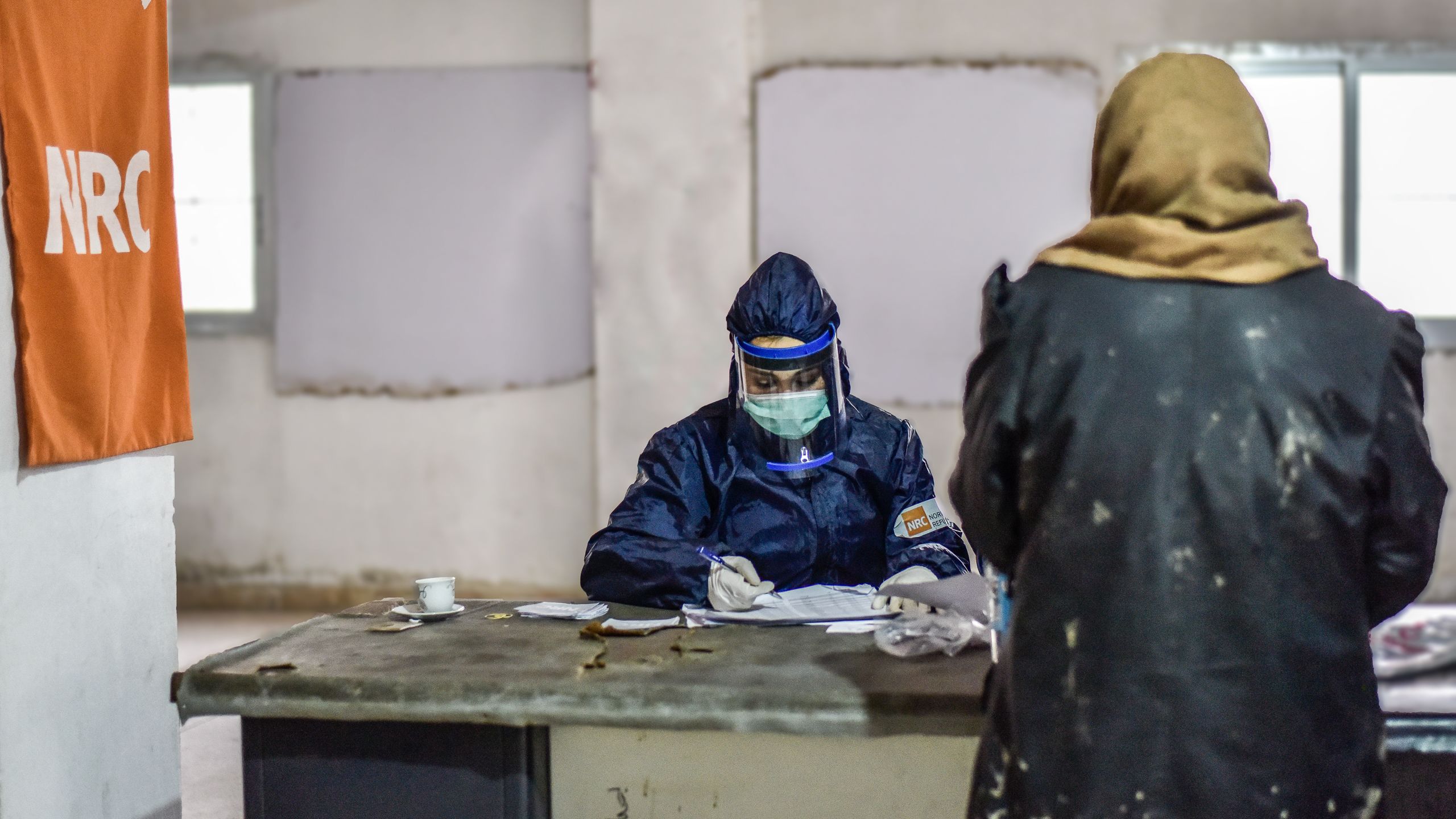 En ansatt i Flyktninghjelpen i fullt smittevernutstyr arbeider med å dele ut bistand til familier i nød.